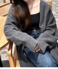 A woman wearing a long, loose-fitting, hooded knitted cardigan in a solid colour, showcasing its below-the-knee length.