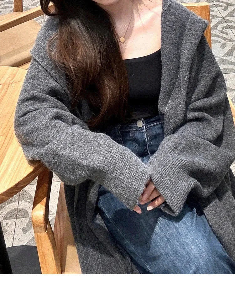 A woman wearing a long, loose-fitting, hooded knitted cardigan in a solid colour, showcasing its below-the-knee length.