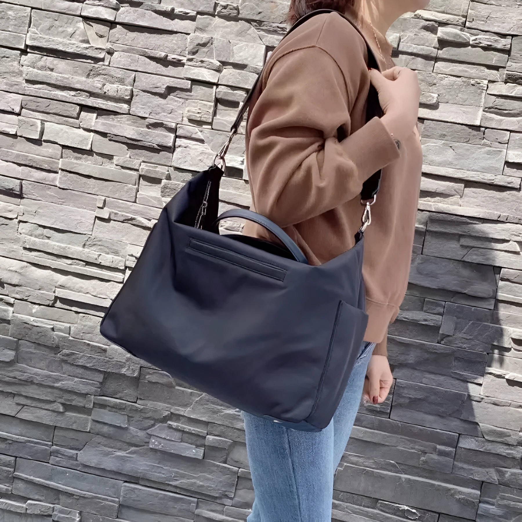 Black waterproof nylon shoulder bag with leather detailing showing large main compartment