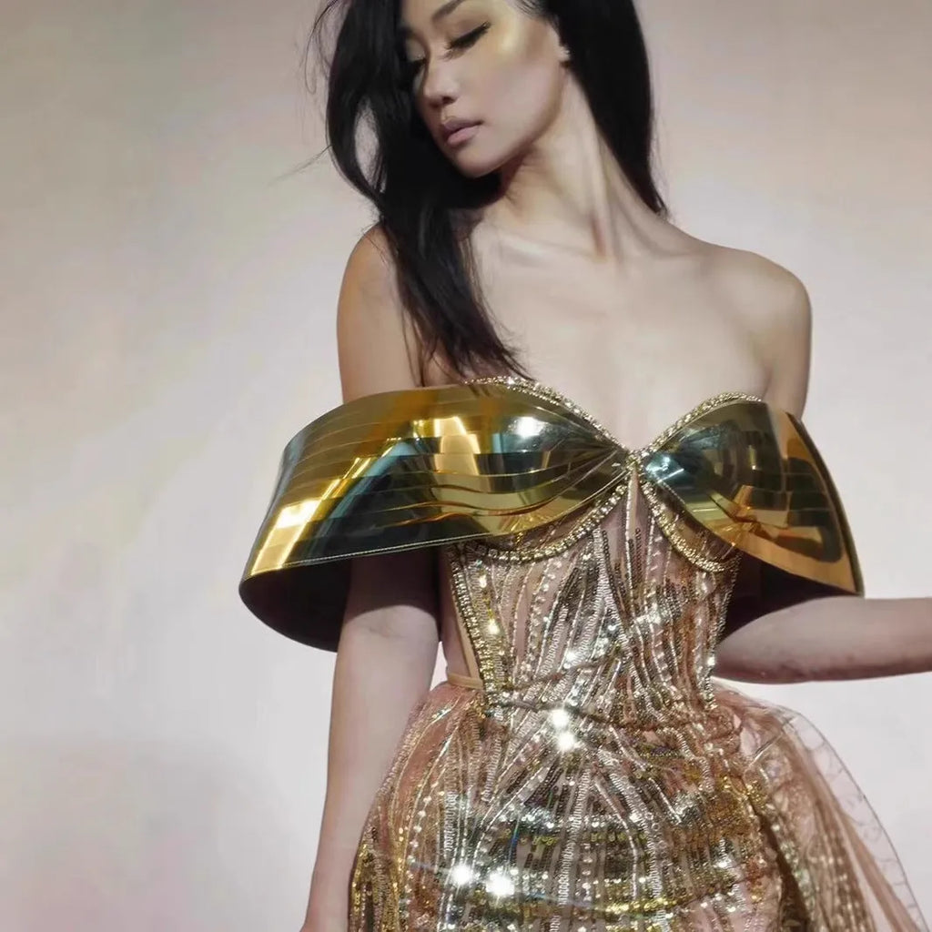 Gold strapless sequin evening dress with a long tulle skirt and thigh split on a mannequin.