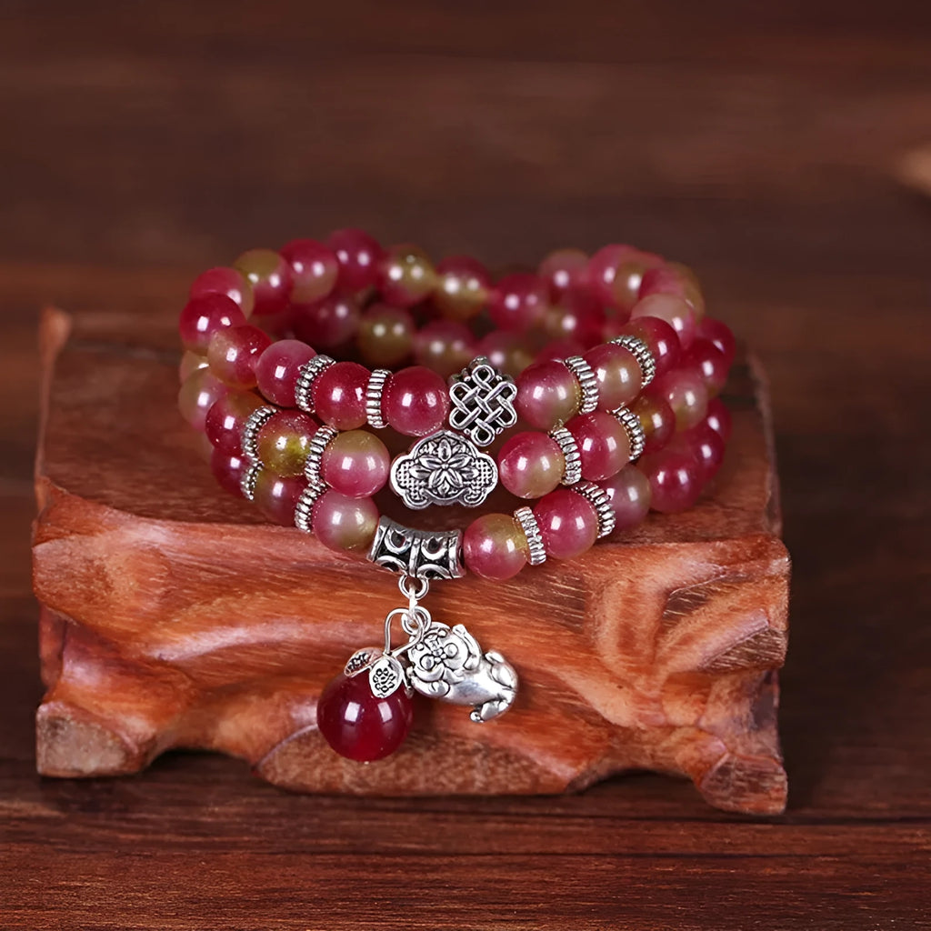 A handmade bracelet with geometrically cut watermelon crystal beads and a red Chinese knot closure on a white background.