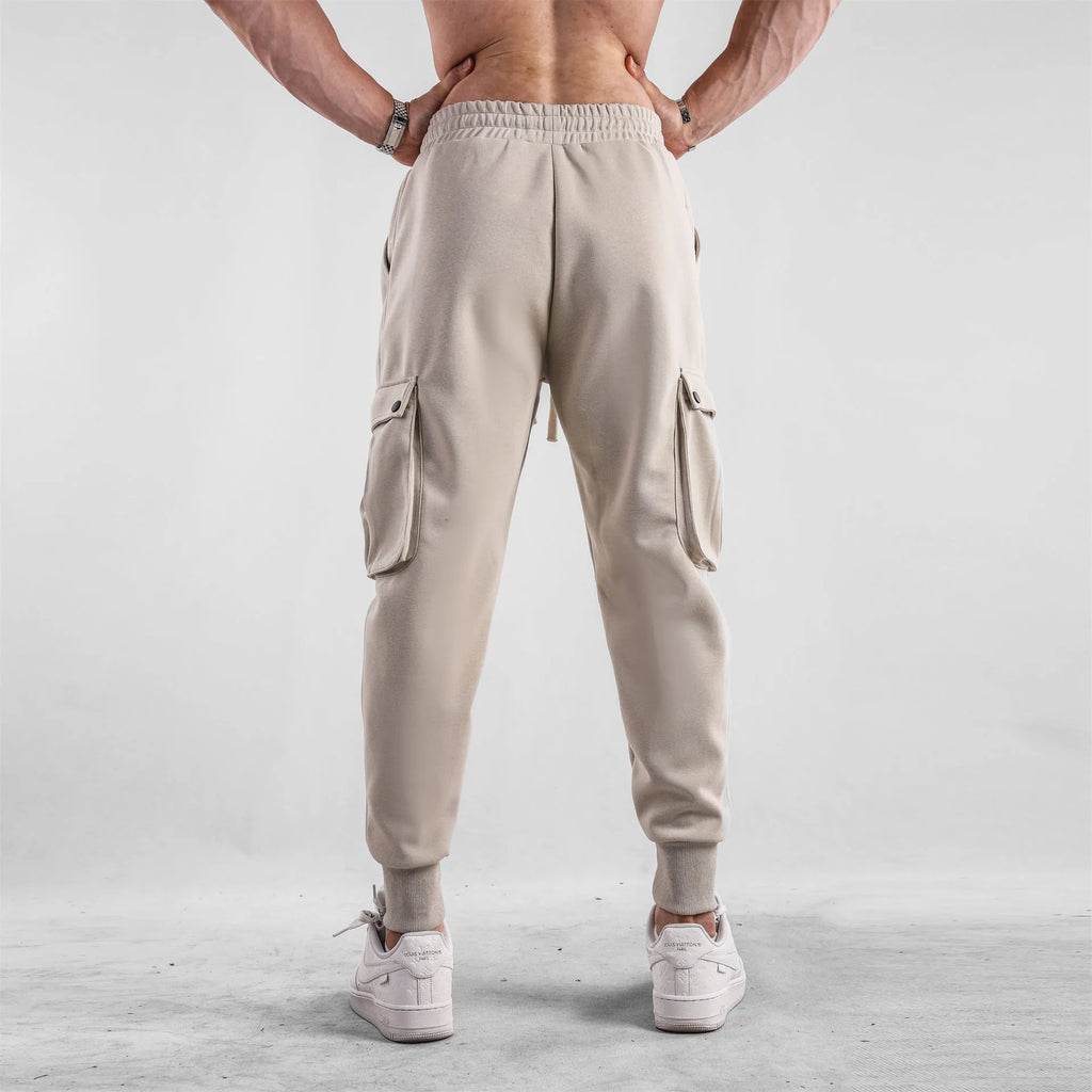 Men's beige ankle-tie loose-fit casual cotton trousers with side pockets on a neutral background.
