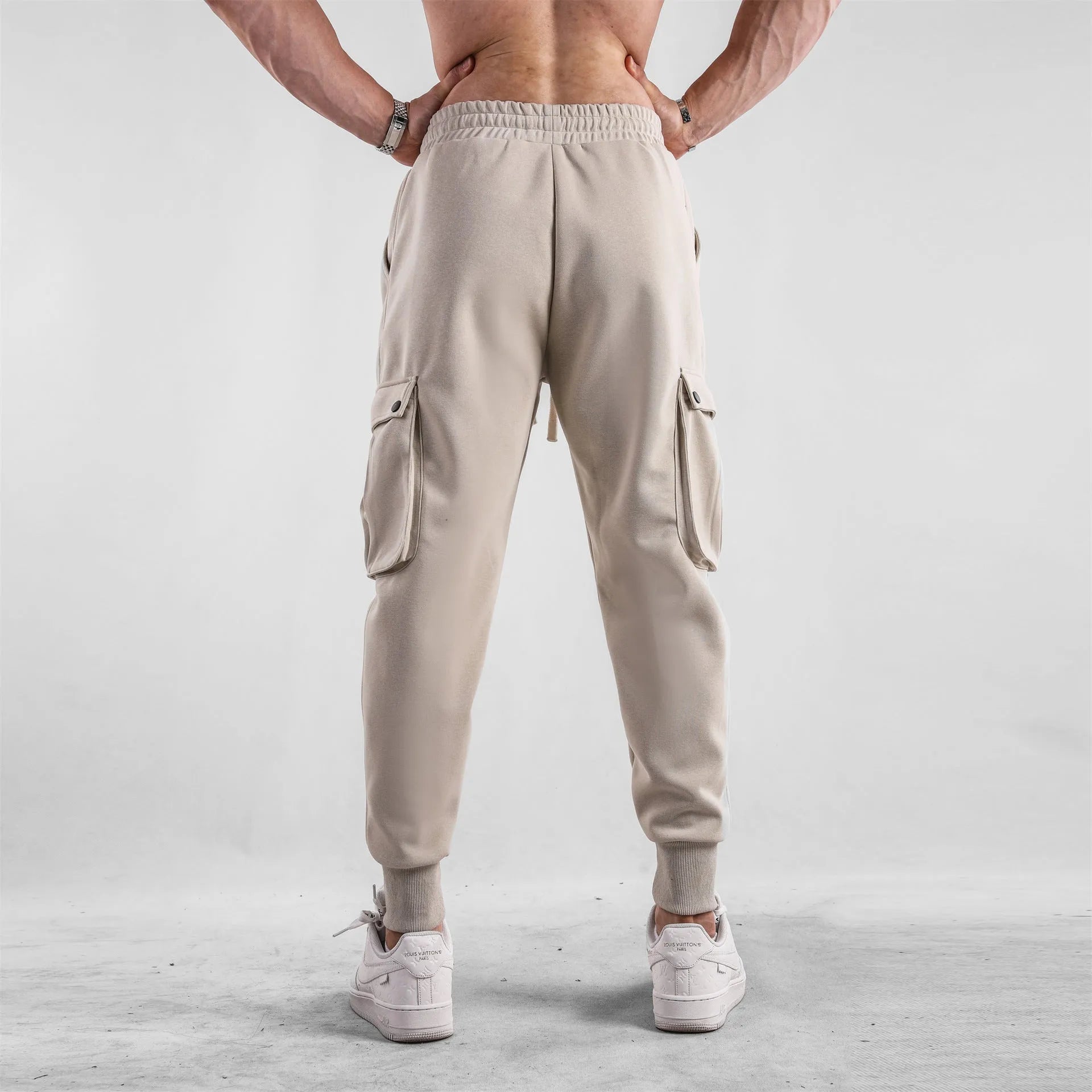 Men's beige ankle-tie loose-fit casual cotton trousers with side pockets on a neutral background.