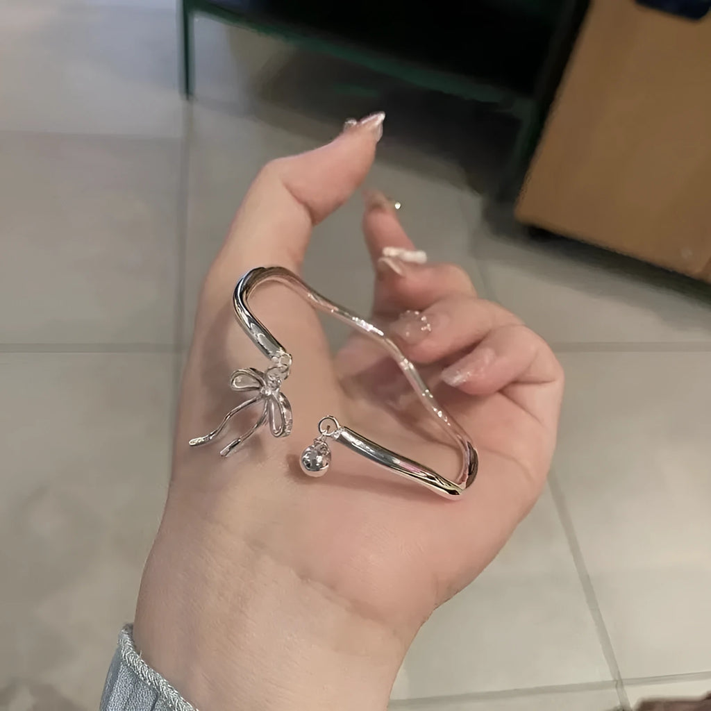 Silver tone adjustable bangle bracelet with a decorative bow charm and lobster clasp on a white background.