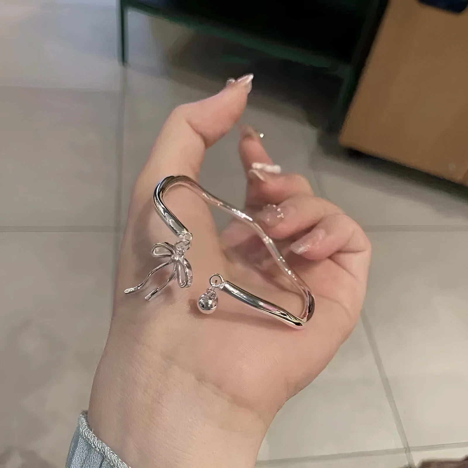Silver tone adjustable bangle bracelet with a decorative bow charm and lobster clasp on a white background.