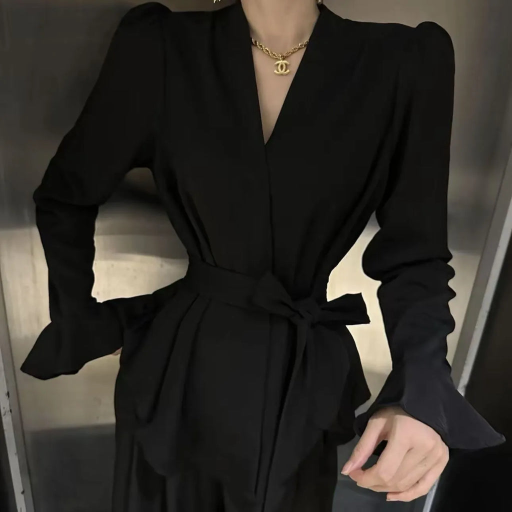 Woman wearing a black French-style shirt with an irregular collar, long bell sleeves, and a tie-front closure.
