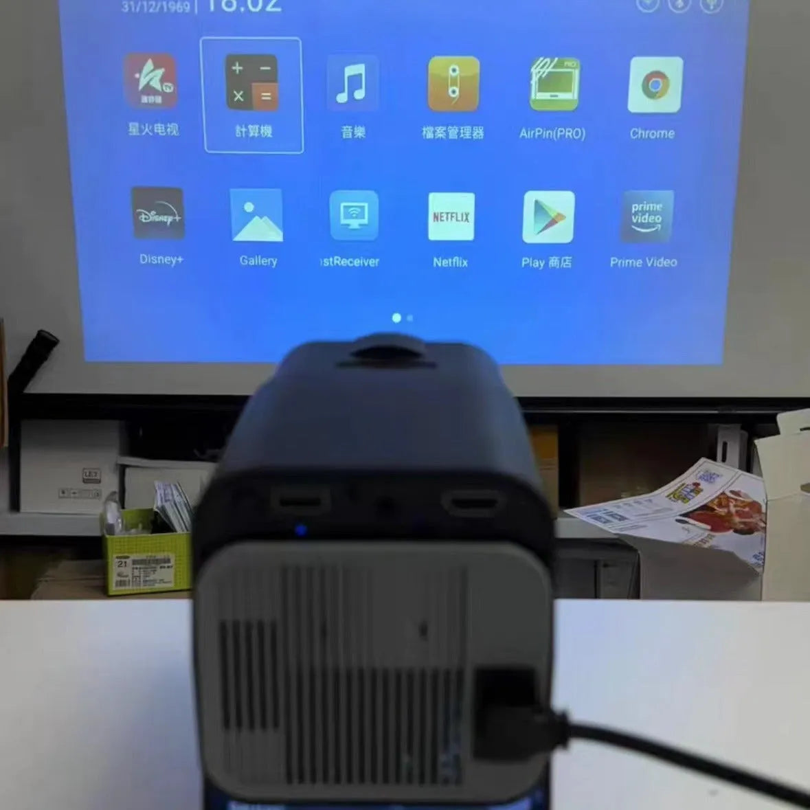 A wireless home projector with a handheld remote on a table, set up for big-screen gaming or movie viewing.