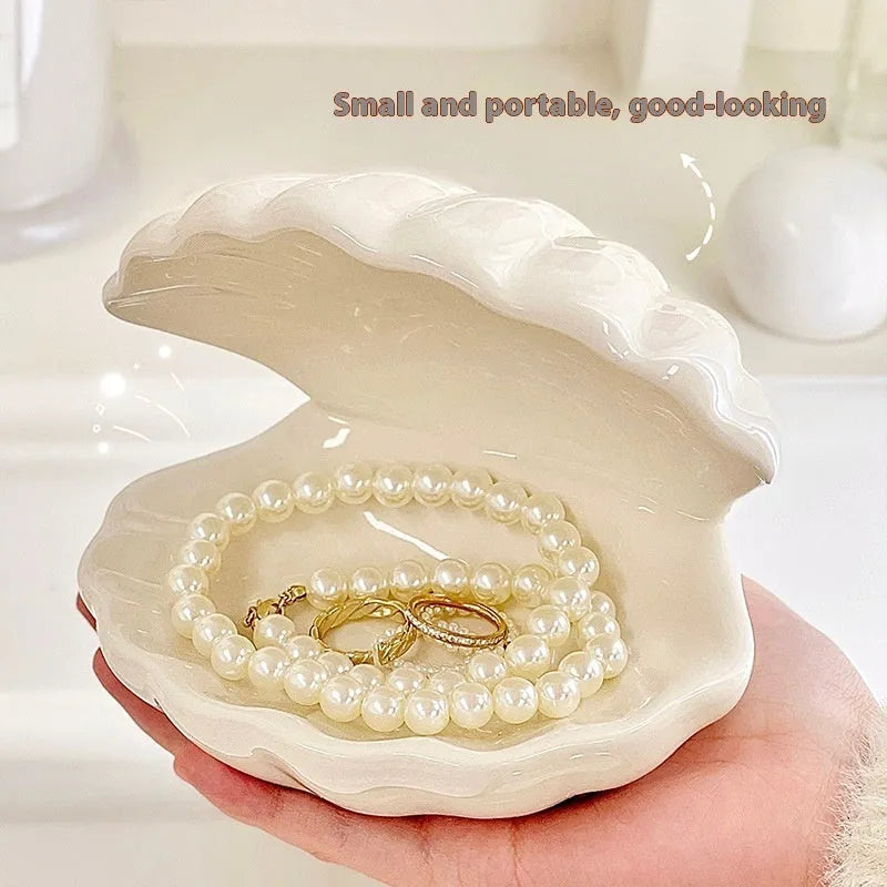 White porcelain scallop shell tray with optional warm LED night light, holding small jewellery on a bedside table.