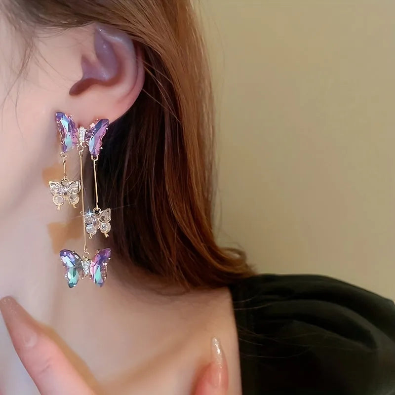 Long silver drop earrings with a blue-purple butterfly, crystal flowers, and a delicate tassel on a white background.