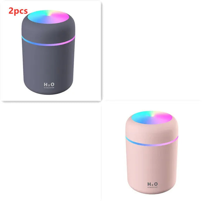 Pink USB mini humidifier with LED lights on wooden desk beside laptop