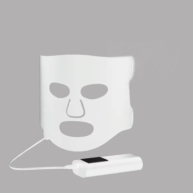 Black and white LED phototherapy face mask with controller and strap on a table.