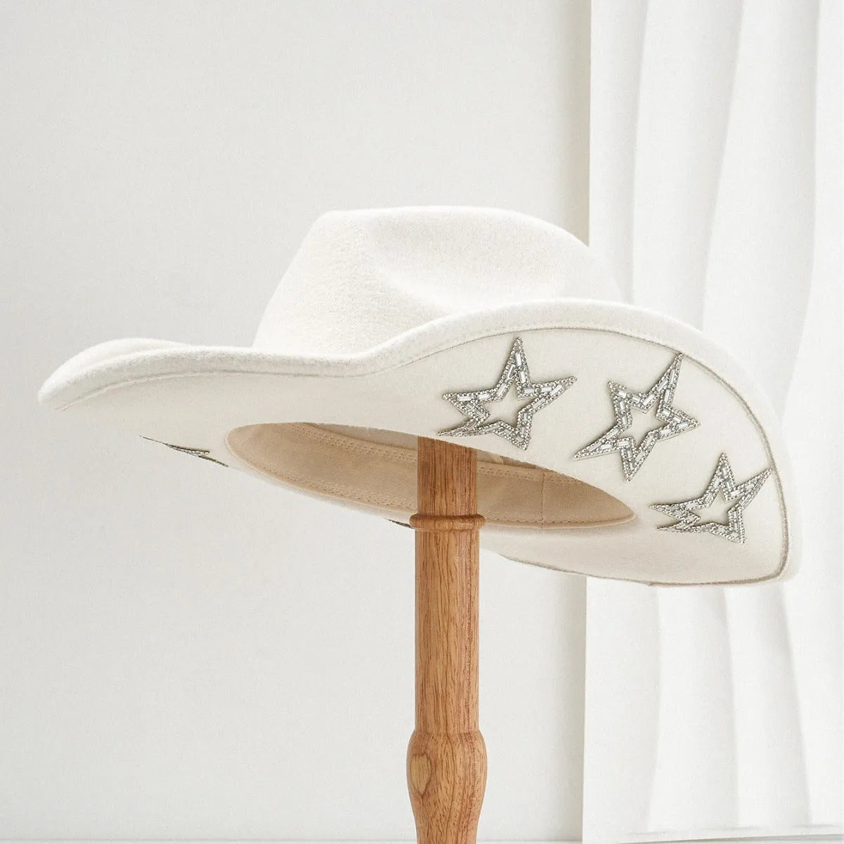 Beige woolen felt western style top hat with a conical crown and a silver hexagonal star decoration on the front.
