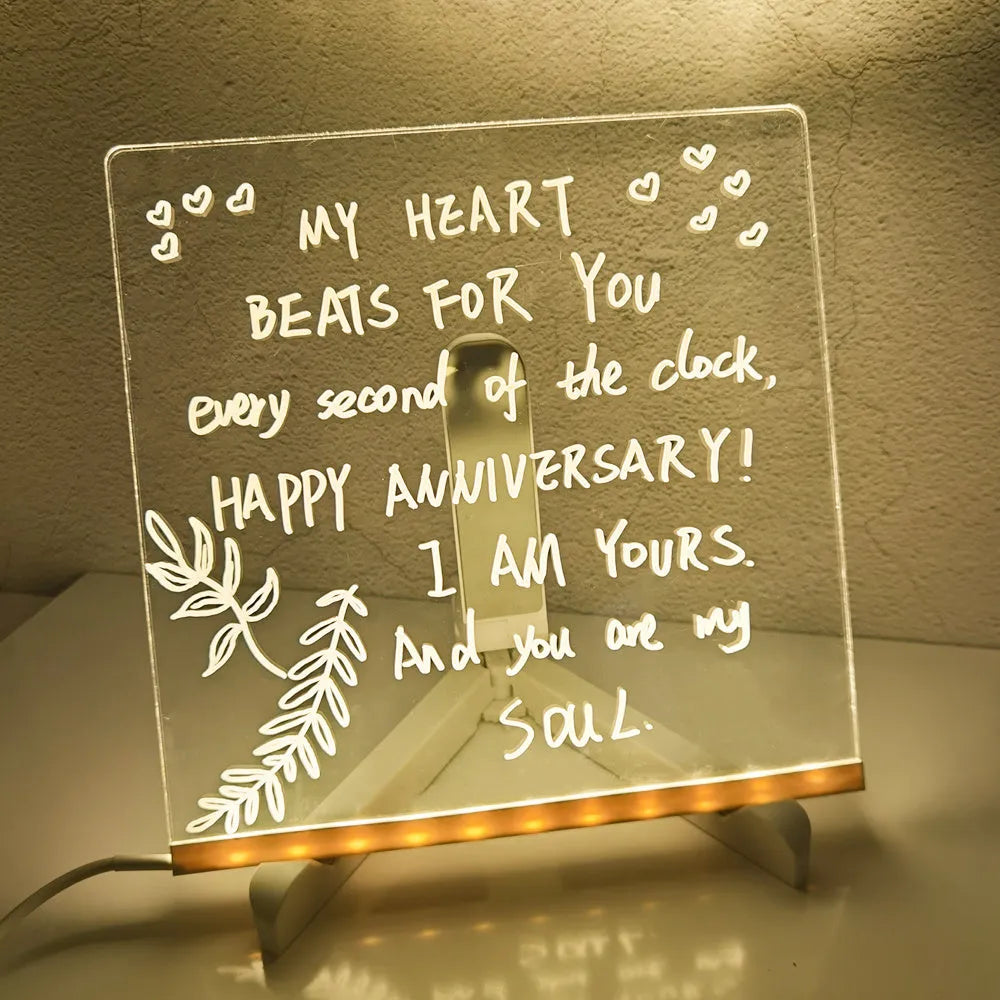DIY acrylic message board LED night light on desk with colourful writing, USB cable, and pens