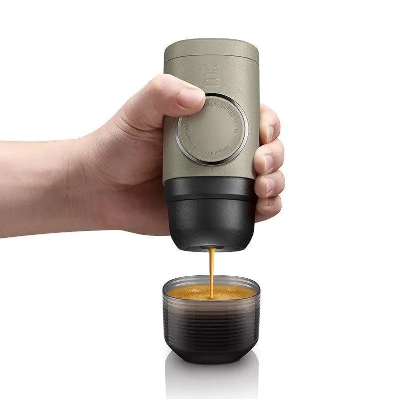 Manual espresso portable capsule coffee machine in olive gray with resin body, 129x70x60mm, on outdoor background