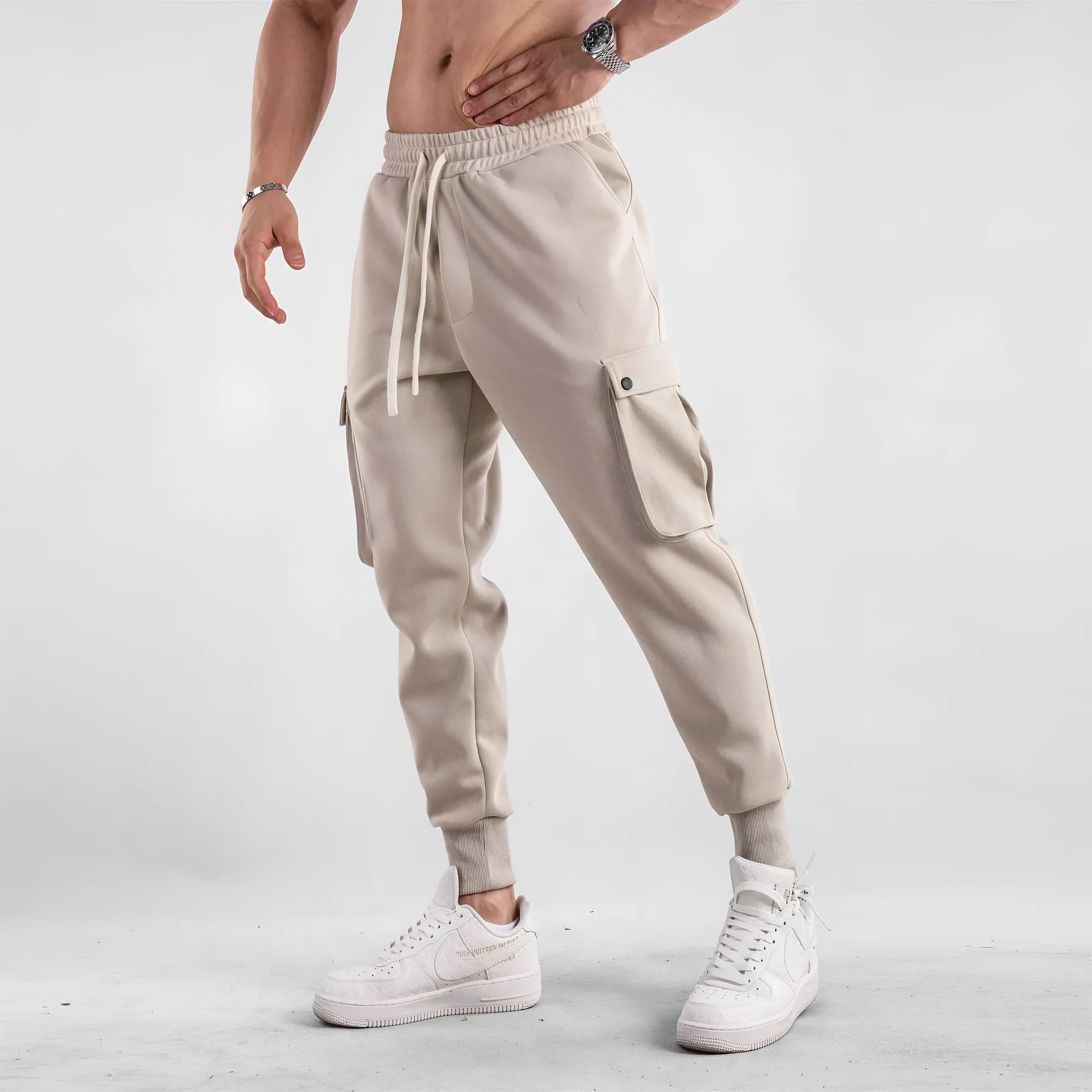 Men's beige ankle-tie loose-fit casual cotton trousers with side pockets on a neutral background.