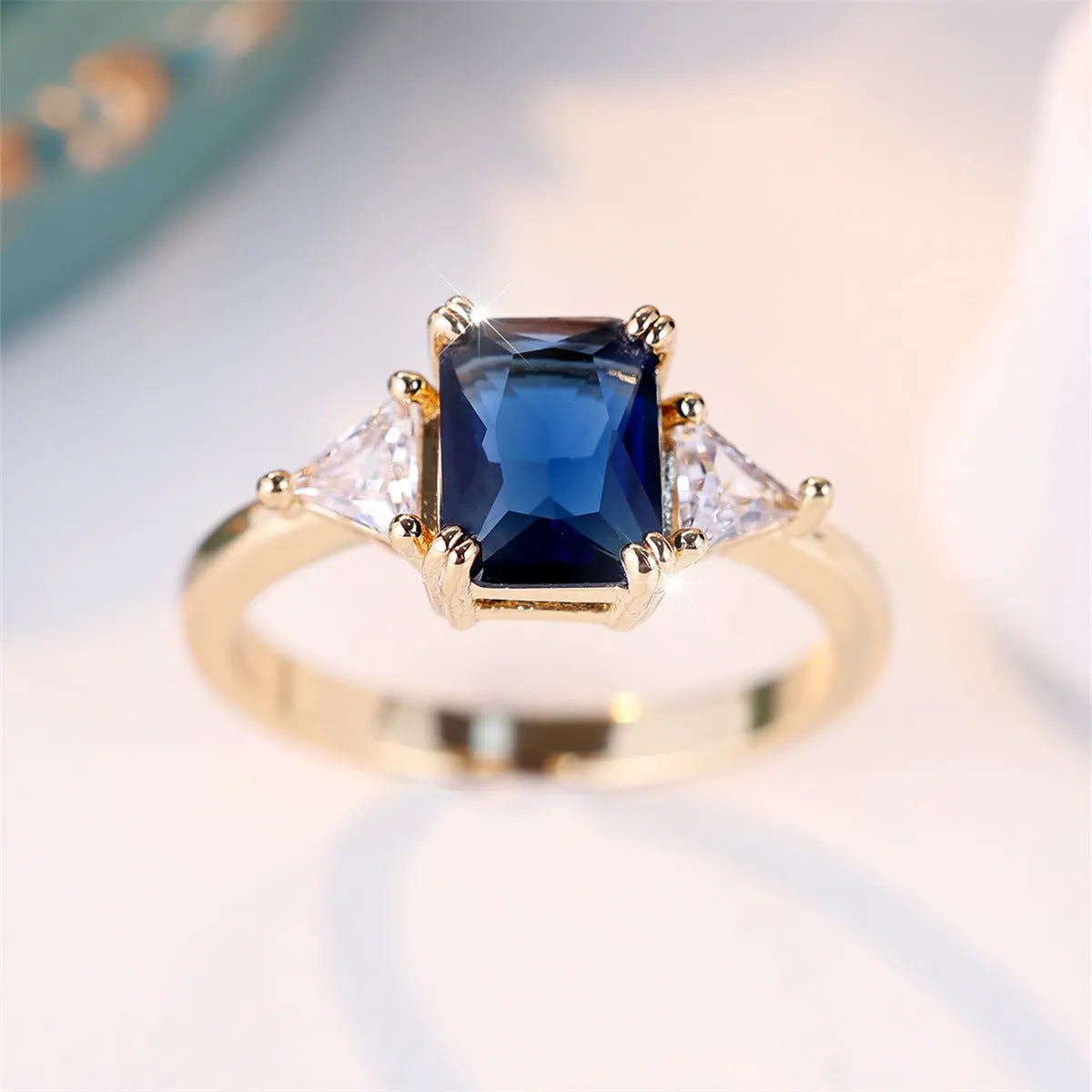 A gold sapphire blue rectangular copper ring for women on a jewellery display.