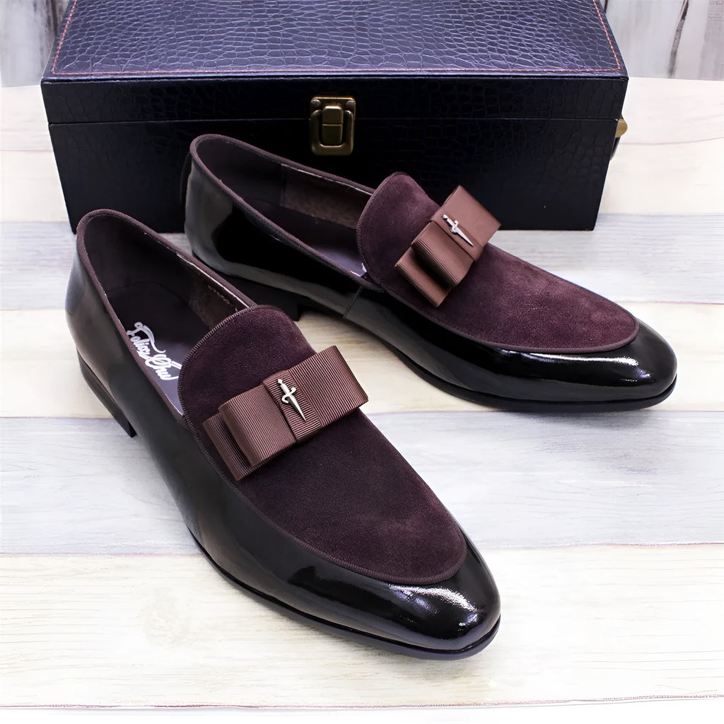 Men's black tassel loafers with matte and glossy patent leather uppers and a rubber sole, shown on a wooden surface.