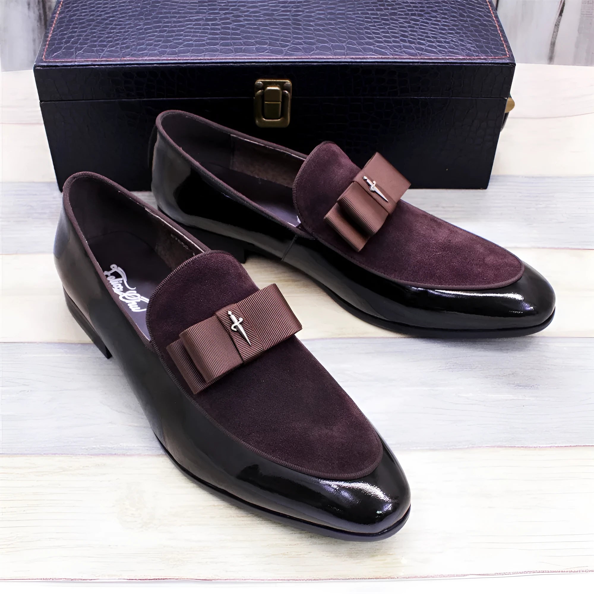 Men's black tassel loafers with matte and glossy patent leather uppers and a rubber sole, shown on a wooden surface.
