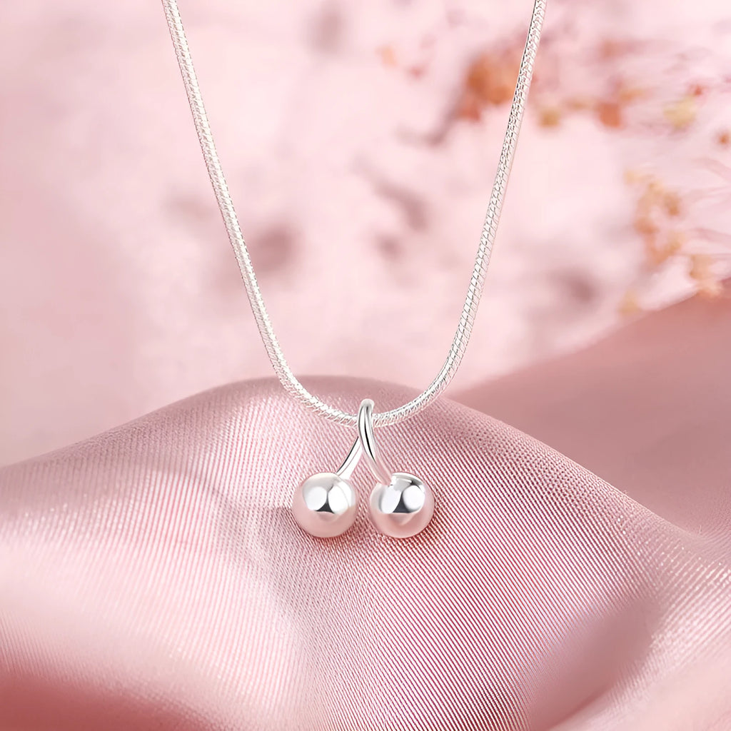 Close-up of a silver cherry pendant necklace on an adjustable snake bone chain, showing the fruit detail and spring ring clasp.