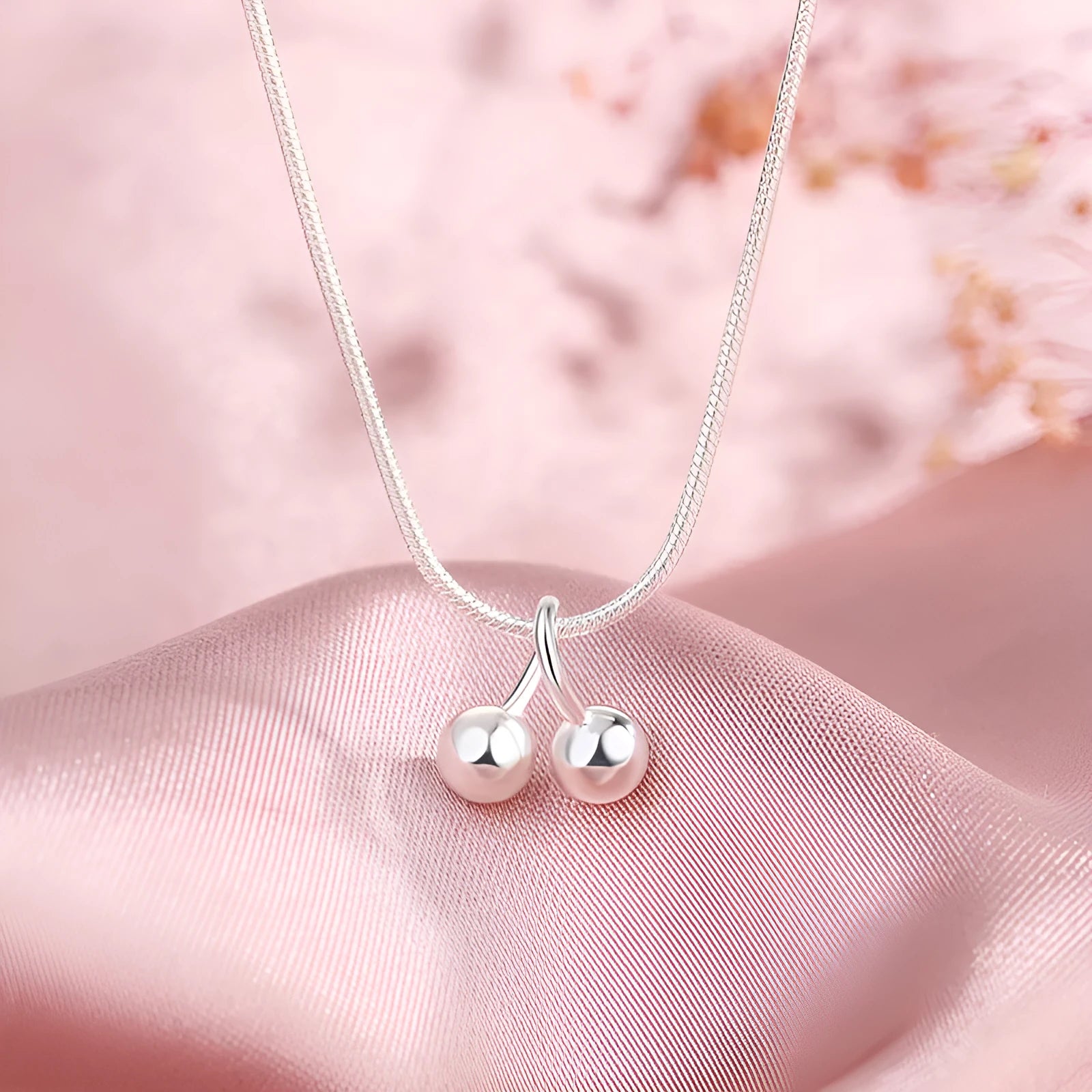 Close-up of a silver cherry pendant necklace on an adjustable snake bone chain, showing the fruit detail and spring ring clasp.