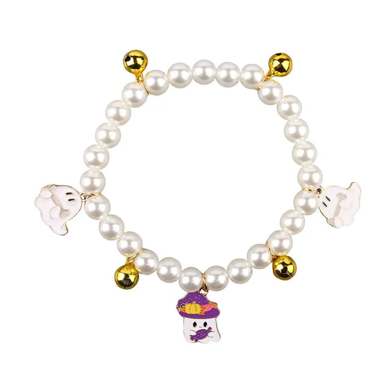 Set of three pet necklaces: a pearl strand, a Halloween cat collar, and a dog bell ornament on a table.