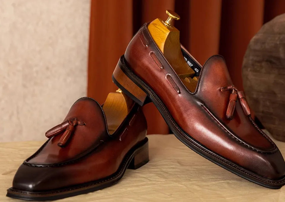 Men's black and brown genuine leather slip-on loafers with a fringed detail and rubber sole.
