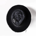 Handmade denim-blue wool felt skull hat with embroidered white skull on front and structured conical crown.