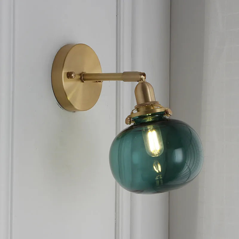 Close-up of a hand-blown pumpkin-shaped glass wall lamp in blue, mounted on a beige wall.