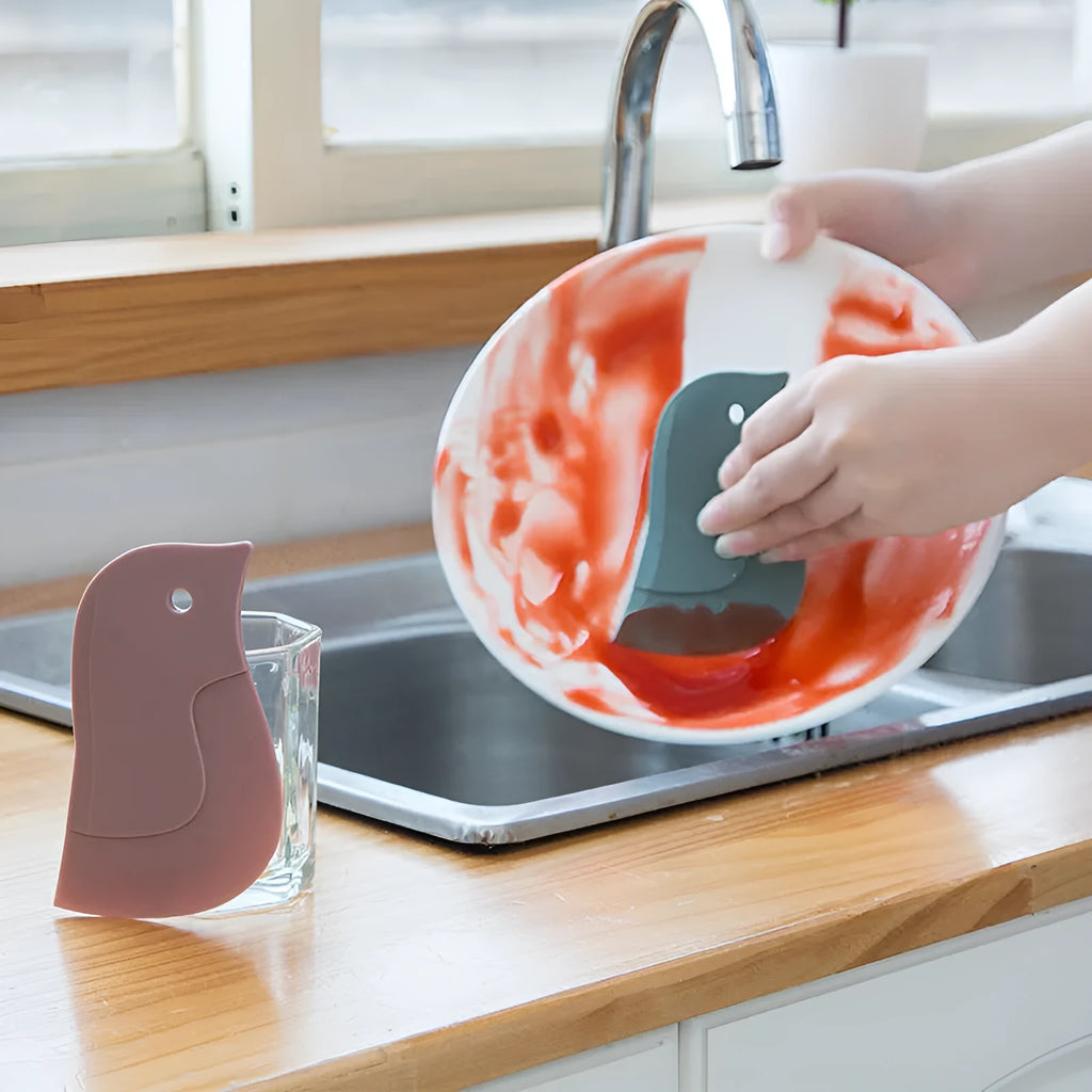 Penguin-shaped soft blade kitchen scraper tool for cleaning plates and pans in green, grey, or pink colours