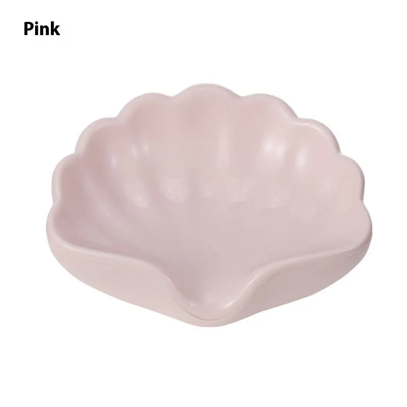 White or pink plastic shell-shaped soap dish with raised design on a bathroom counter.