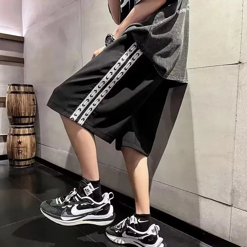 Men's black loose-fit polyester track pants with an elasticated waist, shown in a casual setting.