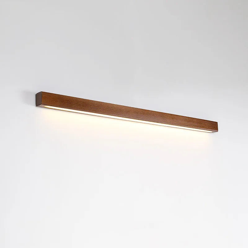 Modern walnut-coloured wood and acrylic log strip wall lamp in three lengths on a white wall.