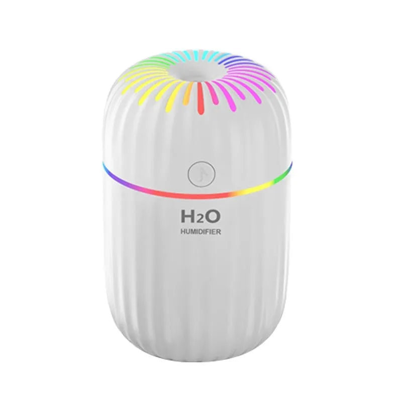 Small white USB humidifier with water tank on a wooden desk next to a laptop.