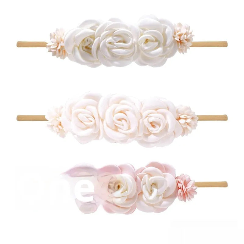 Three cloth flower-shaped hair bands for children in different styles on a light background