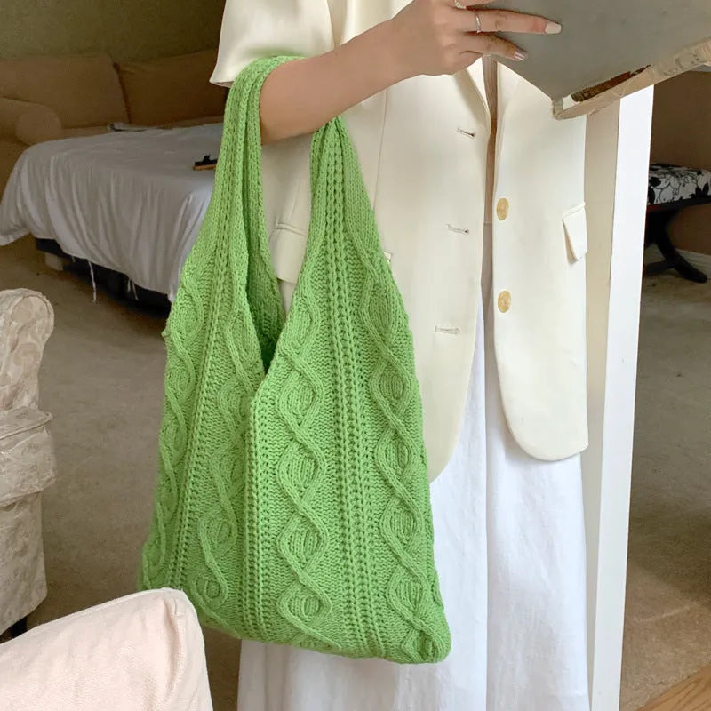 GWomens beige knitted tote bag with double shoulder straps on a wooden table.