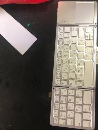 Black tri-fold folding Bluetooth keyboard with touchpad shown open and closed, next to a mobile phone.