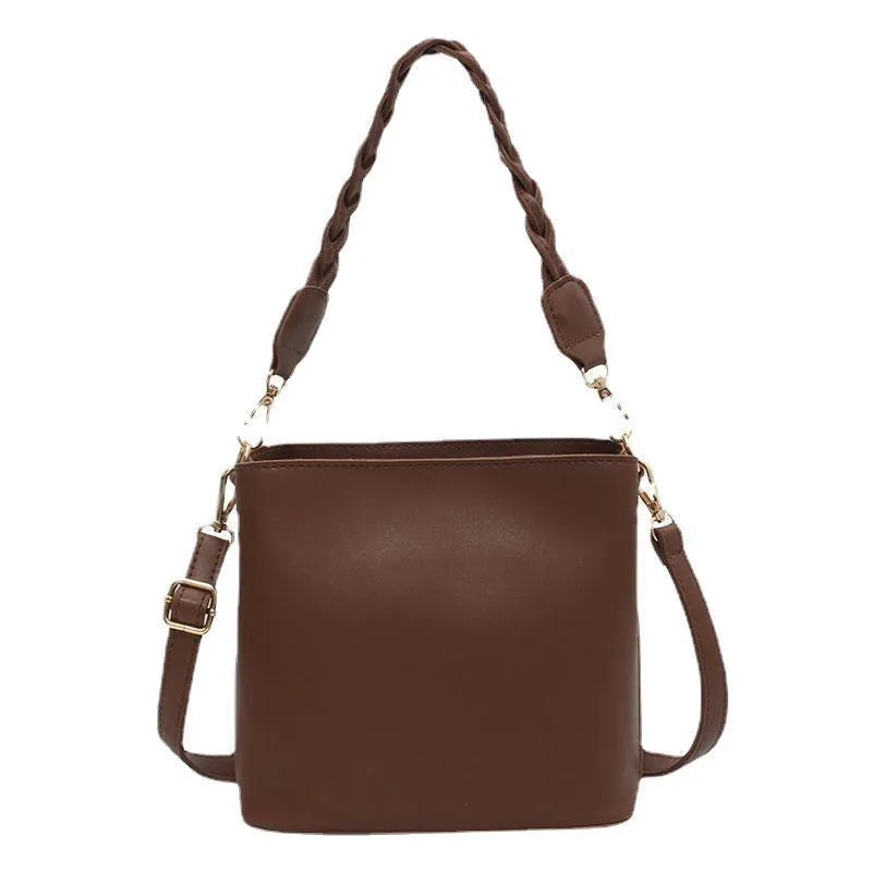 Khaki woven texture one-shoulder crossbody bucket bag with an underarm strap on a table.