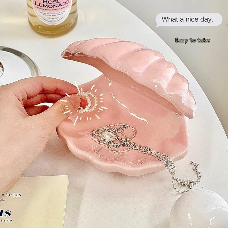 White porcelain scallop shell tray with optional warm LED night light, holding small jewellery on a bedside table.