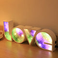 Rainbow-coloured LED LOVE decorative lamp with plastic shell on a table.