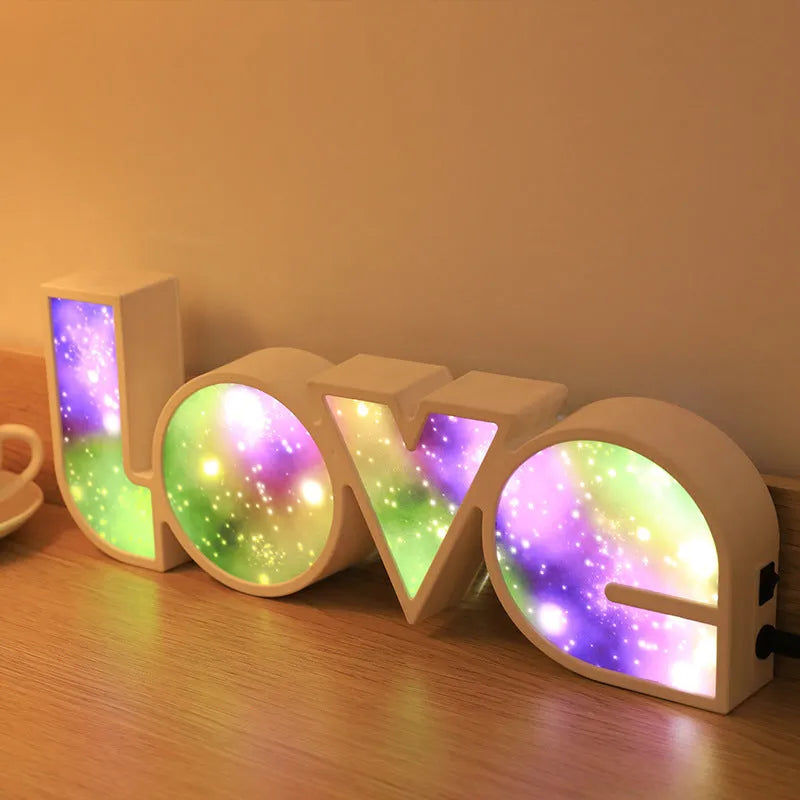 Rainbow-coloured LED LOVE decorative lamp with plastic shell on a table.