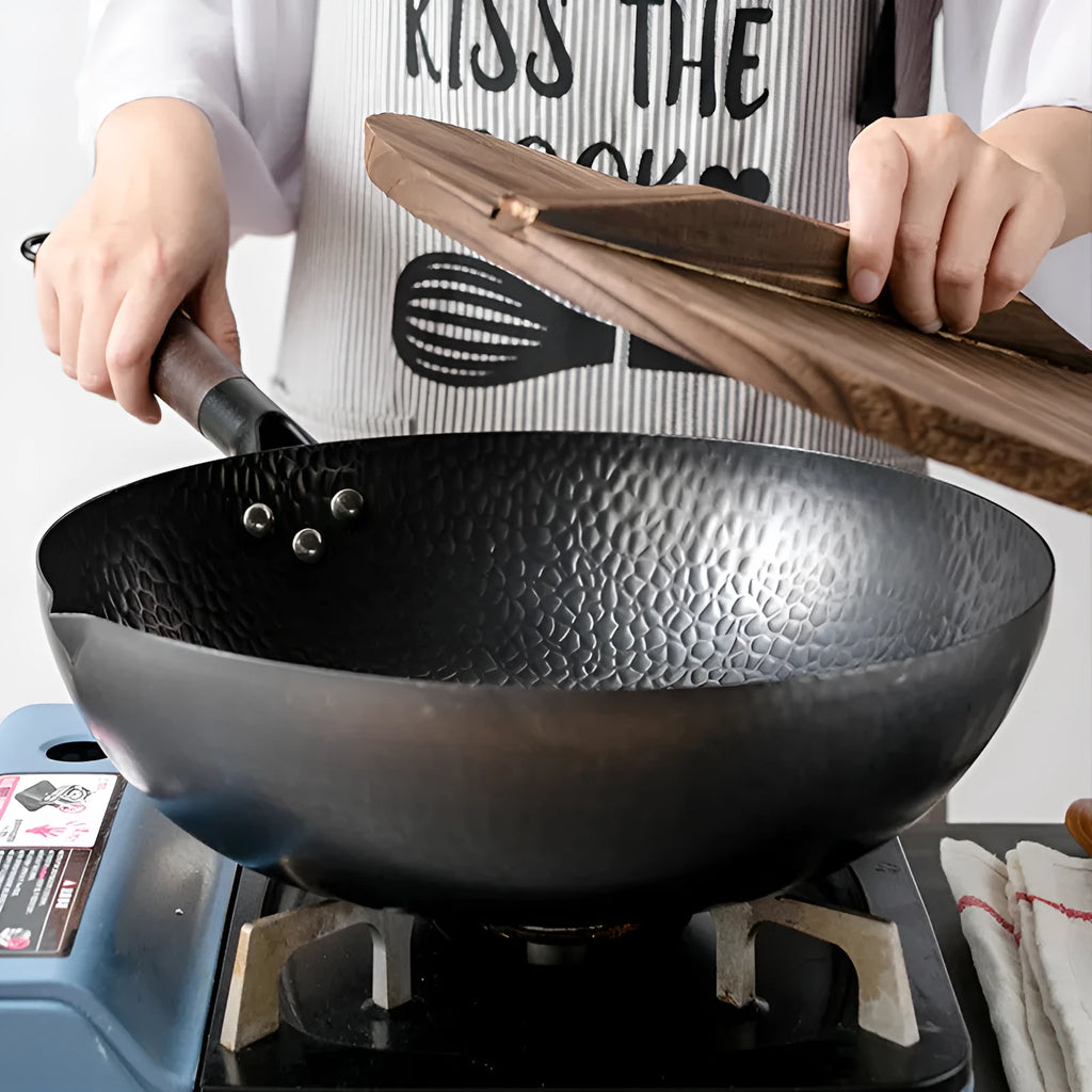 Black traditional cast iron wok with a long wooden handle on a kitchen counter.