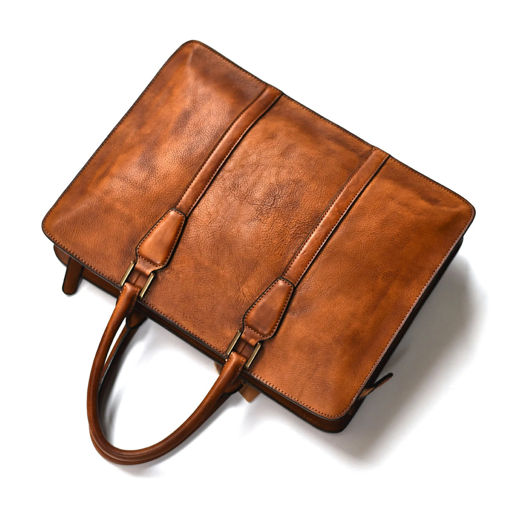 Men's brown leather horizontal business handbag with zipper, shown next to a 14-inch laptop for scale.