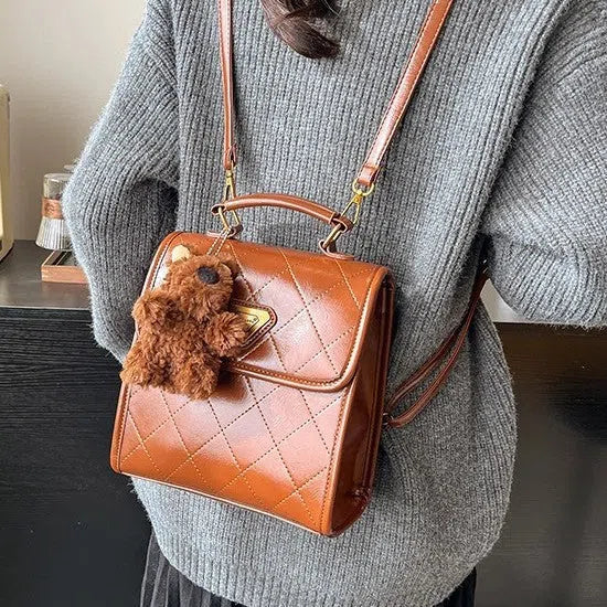 Mini PU backpack in brown with polyester lining, phone pocket, stitching detail, and optional pendant