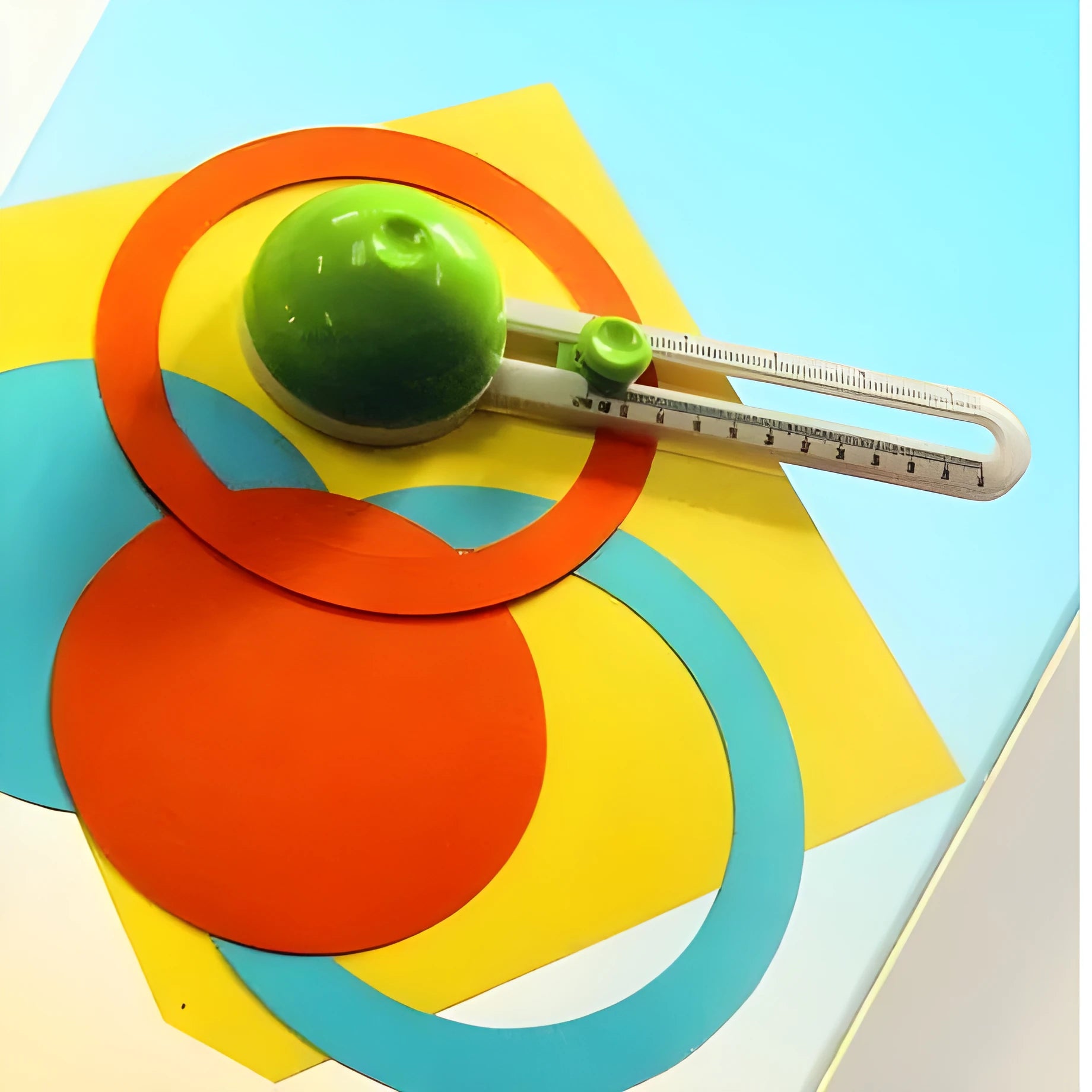 Green and orange plastic round paper cutter for cutting A3 sheets on a desk.