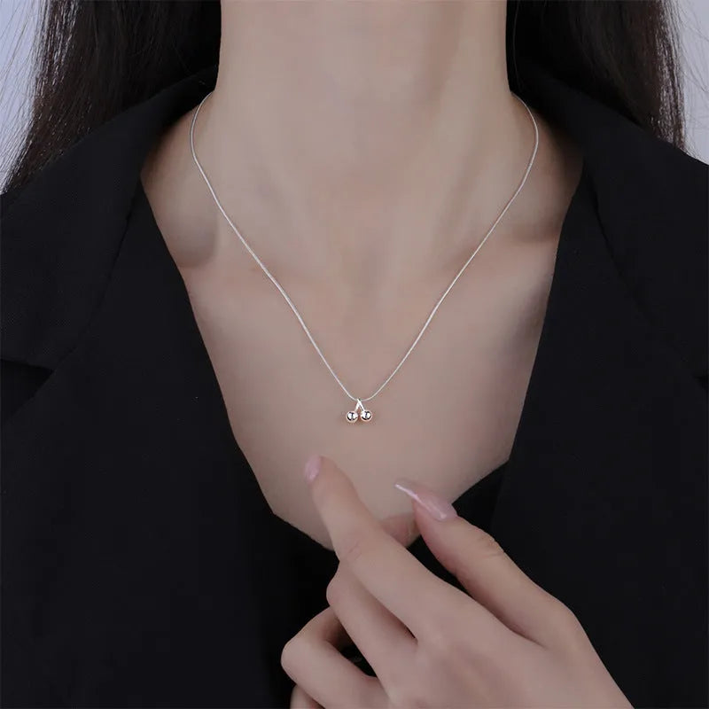 Close-up of a silver cherry pendant necklace on an adjustable snake bone chain, showing the fruit detail and spring ring clasp.