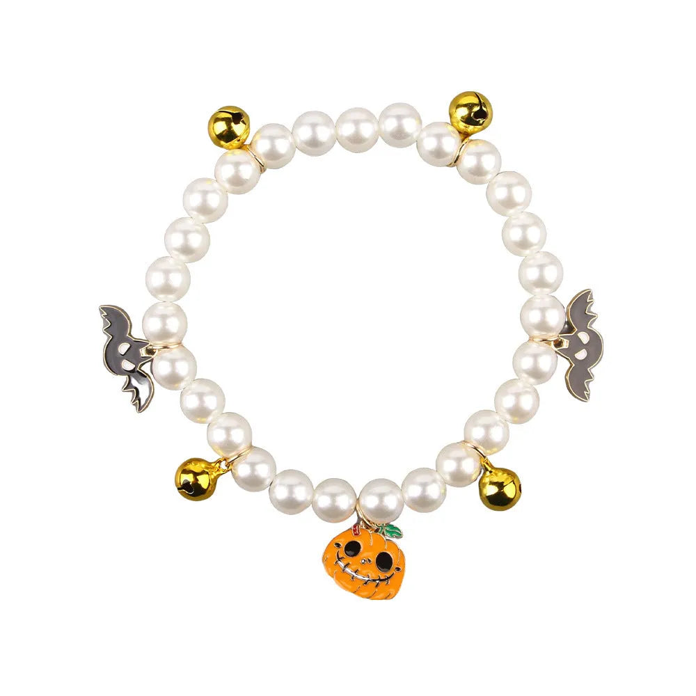 Set of three pet necklaces: a pearl strand, a Halloween cat collar, and a dog bell ornament on a table.