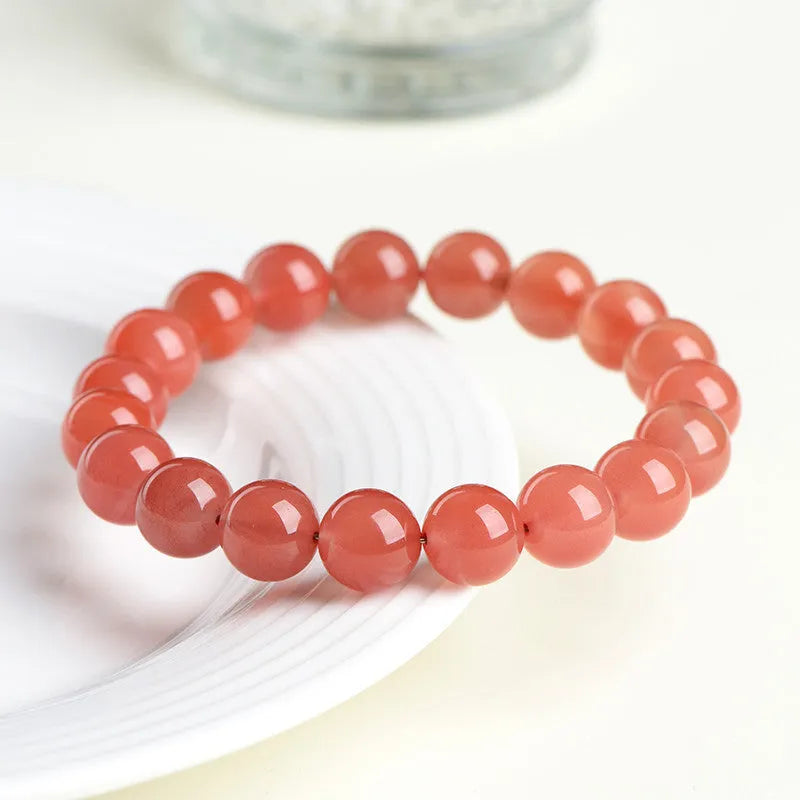 Natural cherry red agate bead bracelet with polished stones on a wrist, showing colour variation and secure clasp.