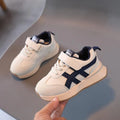 White children's sneakers with Velcro strap and textured rubber sole on a neutral background