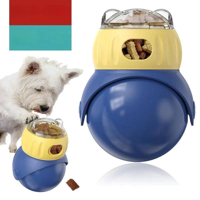 Yellow and blue owl-shaped plastic tumbler toy for cats, a slow-feeder puzzle on a wooden floor.