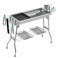 Large stainless steel portable charcoal barbecue oven with iron grill and cooking accessories.